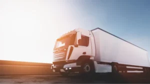 Camión blanco de caja seca circulando por autopista con luz de atardecer y cielo despejado