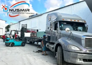 Montacargas cargando mercancía en plataforma de tráiler junto a camión gris en patio industrial